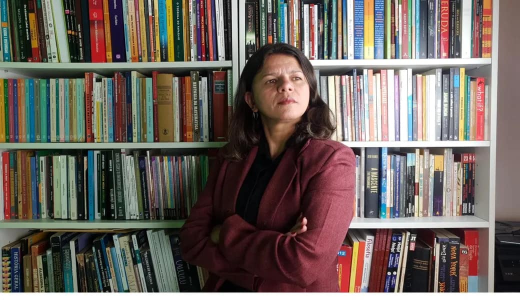 Retrato da Profª Dra. Lessandra Marcelly diante de sua estante de livros